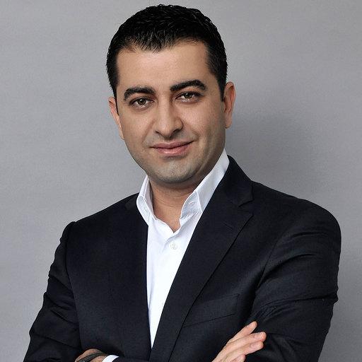 Porträt Andrey Cekovski mit verschränkten Armen, dunkles Sakko und weißes Hemd vor grauem Grund